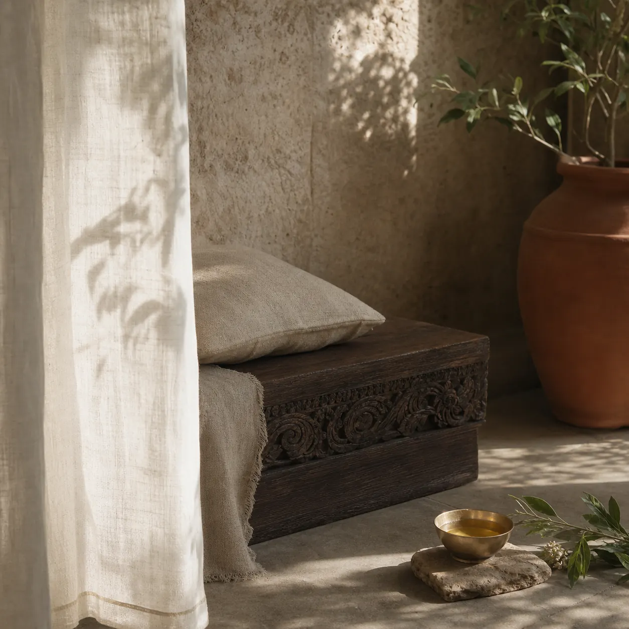 Quiet sanctuary corner with linen, warm stone, carved wood, and botanical shadow